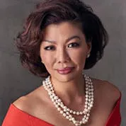 Portrait of a woman with short dark hair, wearing an off-the-shoulder red top and a layered pearl necklace.